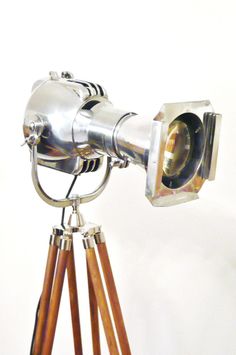 an old fashioned camera on a tripod with wooden legs and a white wall in the background