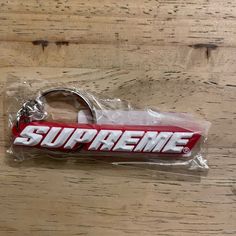 the supreme keychain is wrapped in plastic and sits on top of a wooden table