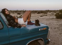 a woman laying on the back of a blue pickup truck in an open desert area