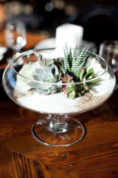 a glass bowl filled with succulents and sand on top of a wooden table