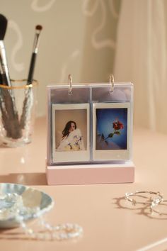 two pictures are attached to the side of a table with jewelry on it and a glass vase behind them