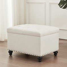 a white ottoman sitting on top of a hard wood floor next to a potted plant