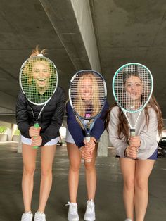 three girls holding tennis rackets in front of their faces and posing for the camera