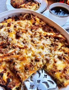 a casserole with meat and cheese is cut into slices on a plate next to two cups of coffee