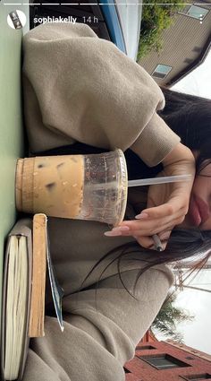 a woman leaning against a wall with an open book and coffee mug in her hand