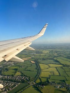 the wing of an airplane flying over green fields and farmlands under a blue sky