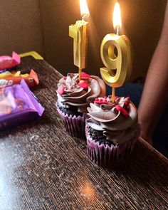 two cupcakes with candles are sitting on a table