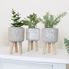 three cement planters with hearts and love painted on them sitting on a white dresser