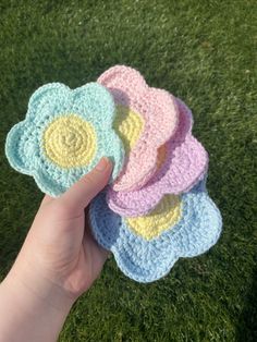 a hand is holding four crocheted flower coasters on the grass in front of someone's hand