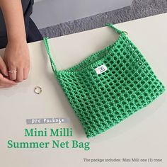 a green crocheted bag sitting on top of a table next to a woman's hand