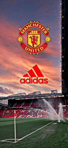 the manchester united logo is sprinkled with water as it stands in front of an empty soccer field