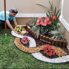 a man kneeling down next to a garden with flowers and plants on the ground in front of him