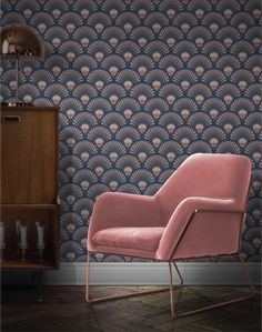 a pink chair sitting in front of a blue wallpaper with an art deco design