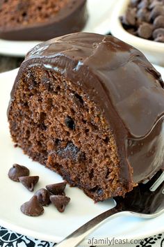 there is a piece of cake with chocolate frosting on the plate and some chocolate chips next to it