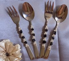 four forks and two spoons with beaded handles on a white table cloth next to a flower