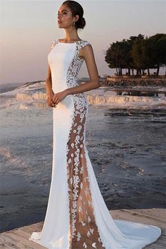 a woman standing on a dock wearing a white and brown dress with flowers in the back