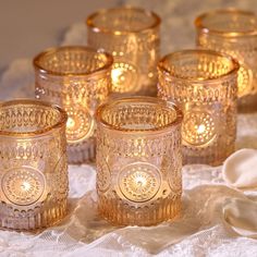 several glass candles are sitting on a lace tablecloth