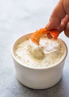 a person dipping something into a small white bowl filled with cream cheese and carrots