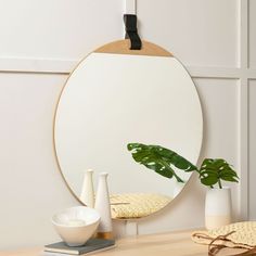 a round mirror sitting on top of a wooden table next to a vase with a plant in it