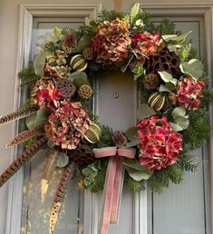 a wreath with flowers and feathers hanging on the front door to decorate it for christmas