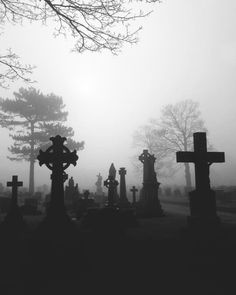 black and white photo of graveyard with crosses in the foreground on a foggy day