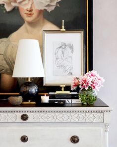 a painting and flowers on a mantle in front of a white mantel with a lamp