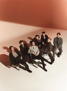 group of men sitting on chairs in front of an orange wall with shadows from the floor