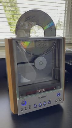 an open cd player sitting on top of a table next to a window with blinds