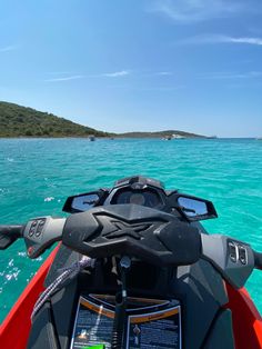 the back end of a boat in clear blue water with an island in the distance