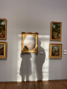 the shadow of a person standing in front of paintings on a wall with wooden floors