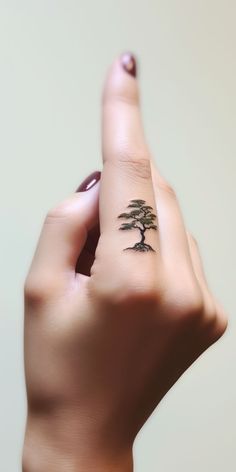 An elegant, minimalistic bonsai tattoo adorns the finger, visually symbolizing the wearer's deep-seated love for nature. Discover our 'TreeTee' Etsy shop – every tee purchased aids our tree-planting mission, aligning your fashion choices with a healthier planet. Under Hand Tattoo, Small Bonsai Tree Tattoo, Finger Tree Tattoo, Music Nature Tattoo, Bonsai Tattoo Minimalist, Tree Of Knowledge Tattoo, Bonsai Tree Tattoo, Consciousness Tattoo, Bonsai Tattoo