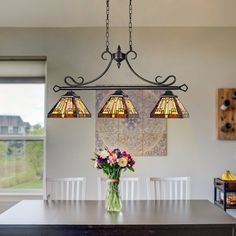 a dining room table with flowers in a vase on it and three lights hanging from the ceiling