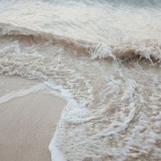 the waves are coming in from the ocean onto the beach sand and white foamy water