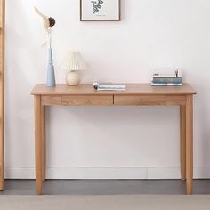 a wooden table sitting in front of a white wall next to a vase with flowers on it