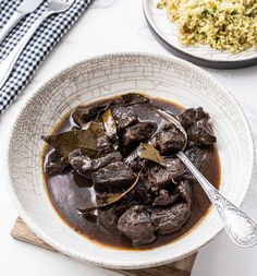 a white bowl filled with beef and brown gravy next to a plate of rice