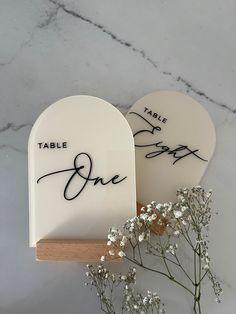 two white heart shaped table numbers sitting on top of a wooden stand next to flowers