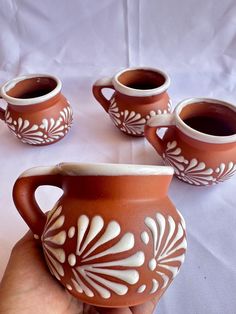 a hand is holding a brown and white vase with four cups in front of it