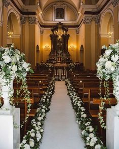 an aisle lined with white flowers and greenery in front of a church pews