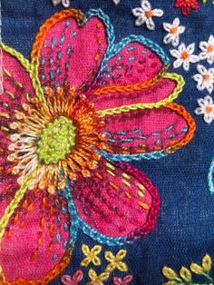 an embroidered flower on blue fabric with white and pink flowers in the center, surrounded by multi - colored threadwork