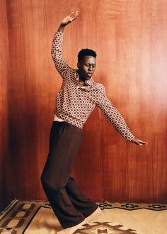 a woman is dancing in front of a wood paneled wall with her arms stretched out