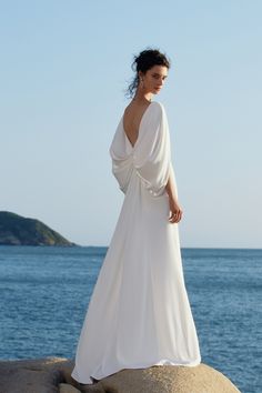 a woman standing on top of a rock next to the ocean wearing a white dress