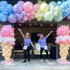 two women standing in front of an arch with balloons and confetti on it