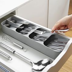 a person is holding a spoon and fork in a drawer with utensils on it