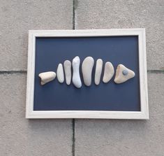 four white and one blue sea glass pieces in a shadow box on the ground next to a brick wall