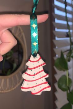 a hand holding a christmas tree ornament on a green string with white and red stripes