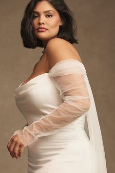 a woman in a white wedding dress posing for a photo with her veil over her shoulder