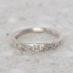 a white gold wedding ring with five diamonds on it's side, sitting on a marble surface