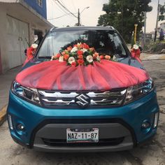 a blue car with flowers on the hood is parked in front of a building and it's covered by a red tarp