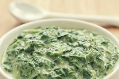 a white bowl filled with green soup on top of a wooden table