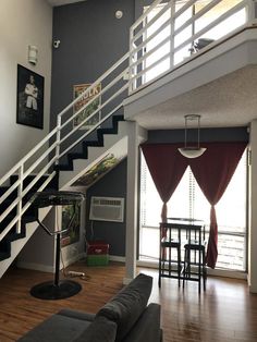 a living room filled with furniture and a stair case next to a kitchen table on top of a hard wood floor